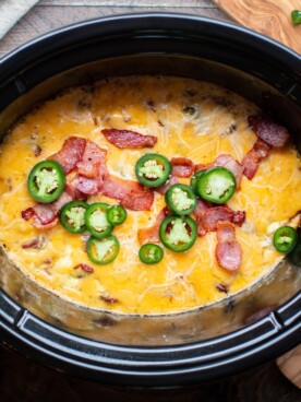 cooked egg casserole in a slow cooker with bacon and jalapenos on top.