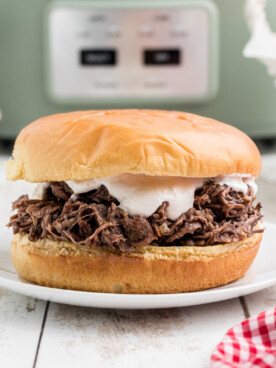 Shredded beef sandwich on a plate with horseradish sauce on it.
