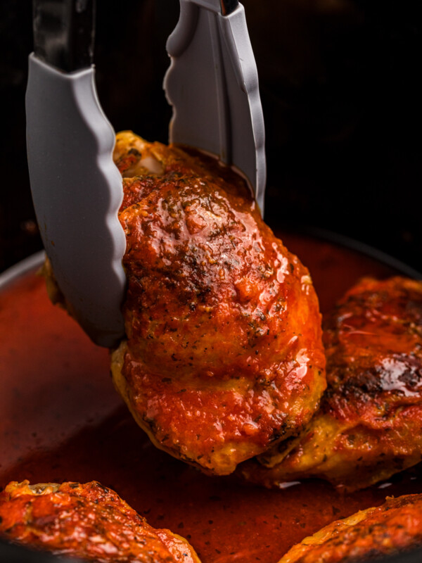 tongs holding a piece of slow cooker hot chicken.