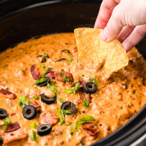 scooping loaded nacho dip with a tortilla chip from a slow cooker.